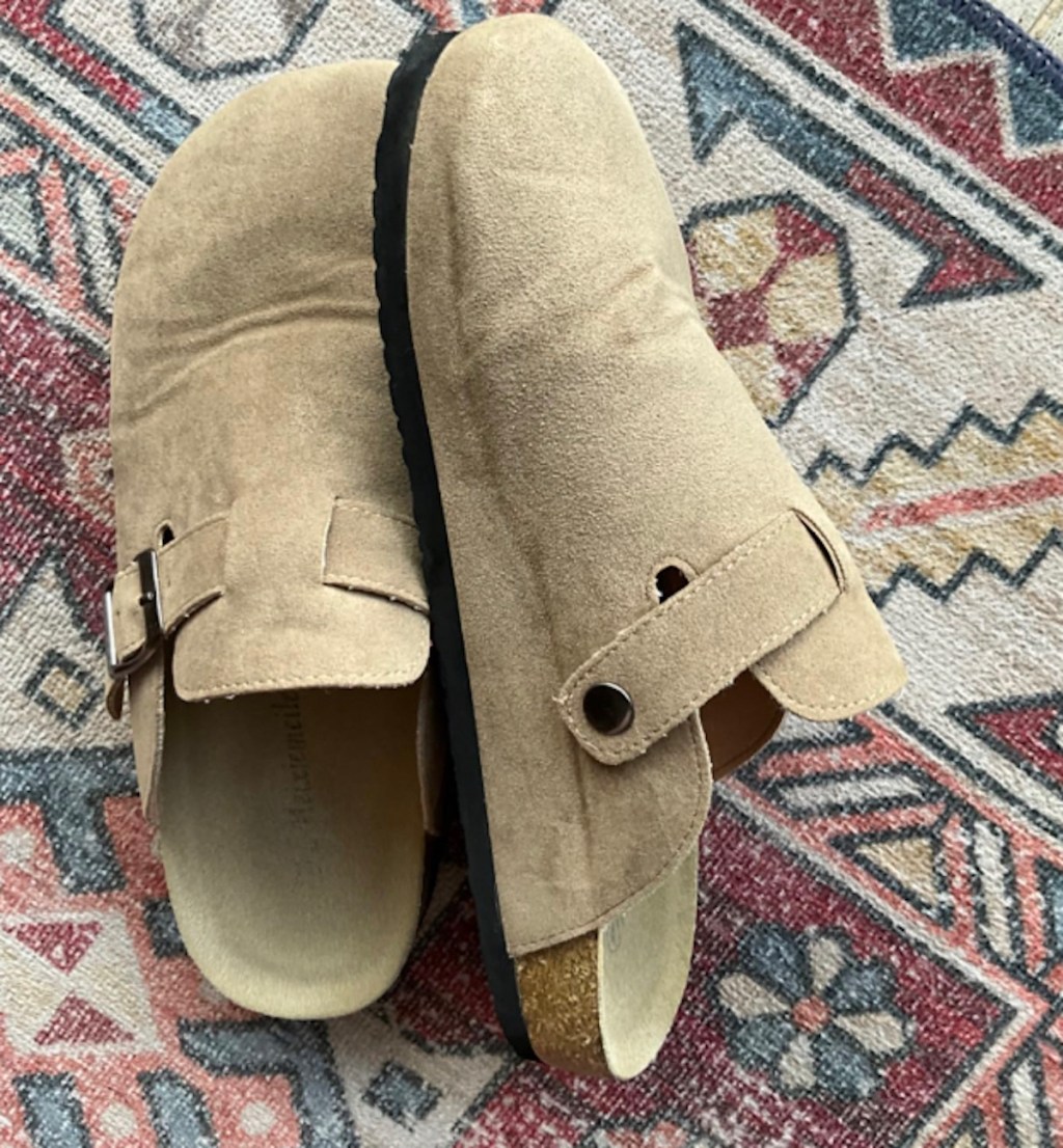 close up of beige suede clogs on patterned rug