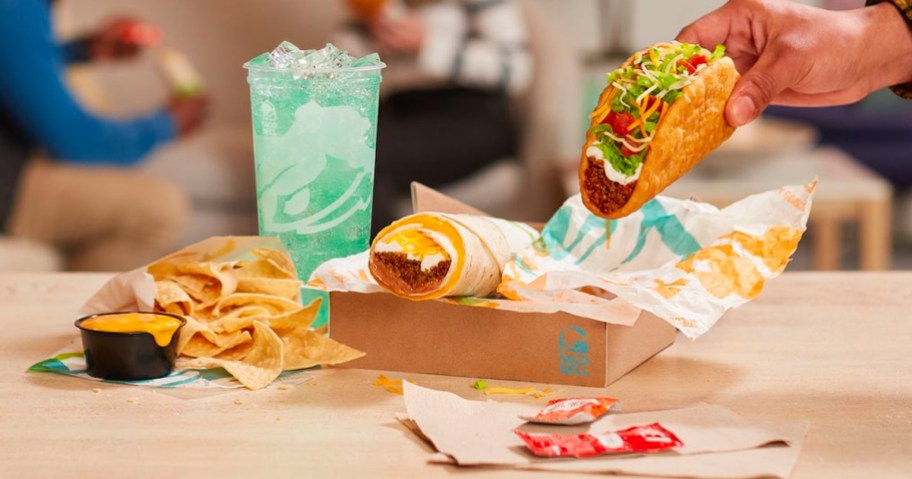 hand holding taco over taco bell cravings items on table