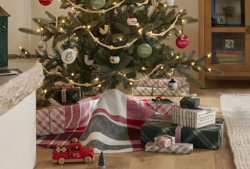 christmas tree with various gifts under it with plaid skirt