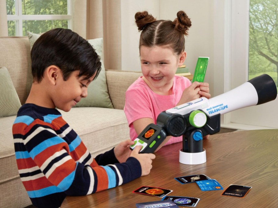 two kids playing with their leapfrog telescope on the floor with cards on the table