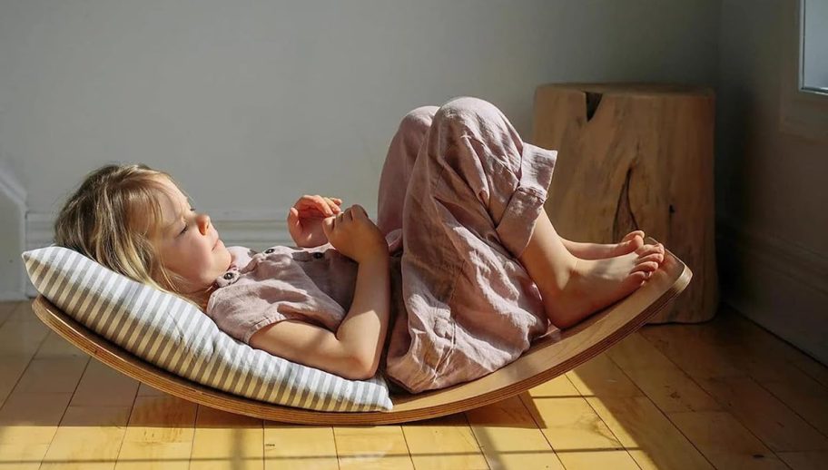 girl laying on balance board on wood floor with pillow