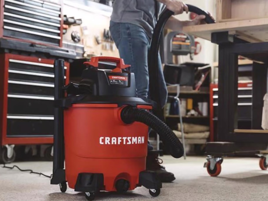 a red and black Craftsman 9 Gal. Corded Wet/Dry Vacuum in workshop, man using it on a work table