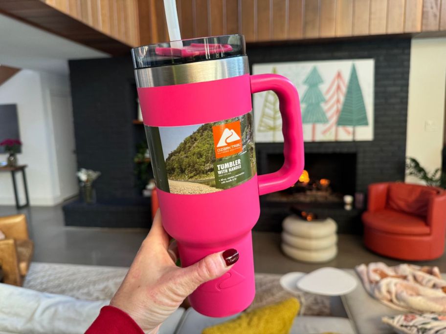 hand holding a Hot Pink Ozark Trail Tumbler with living room in background