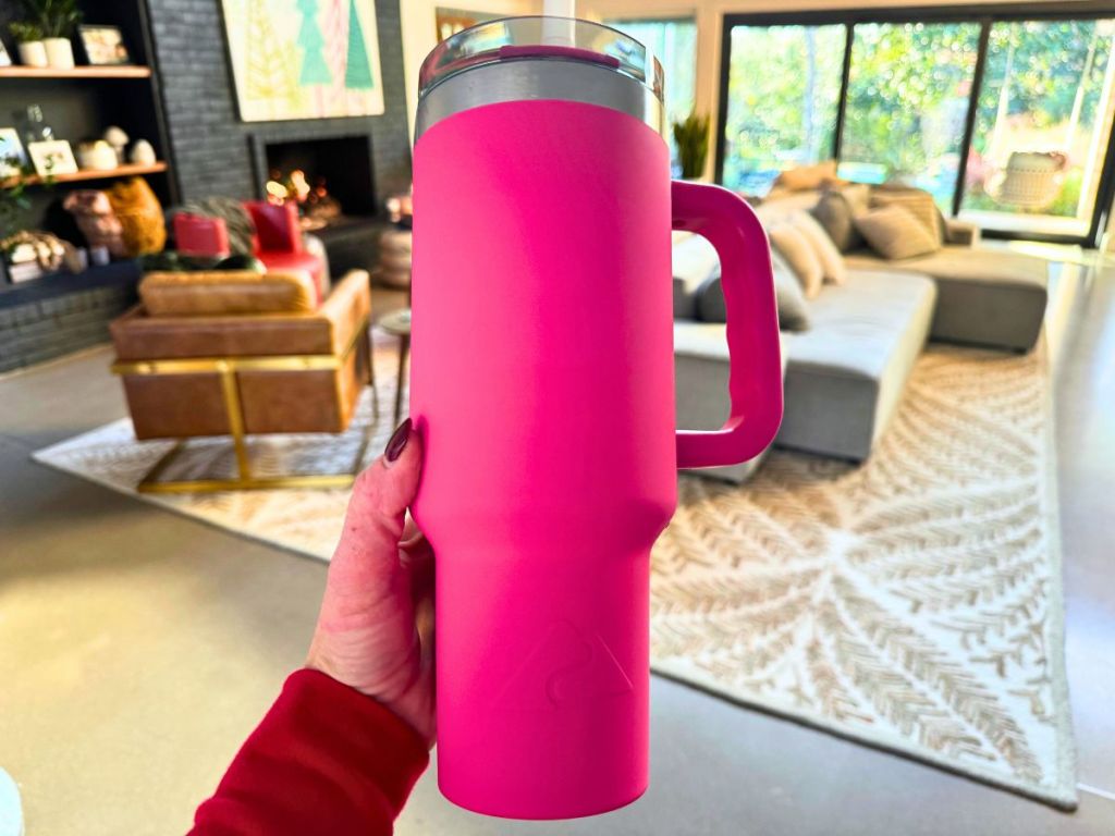 hand holding a Hot Pink Ozark Trail Tumbler with living room in background