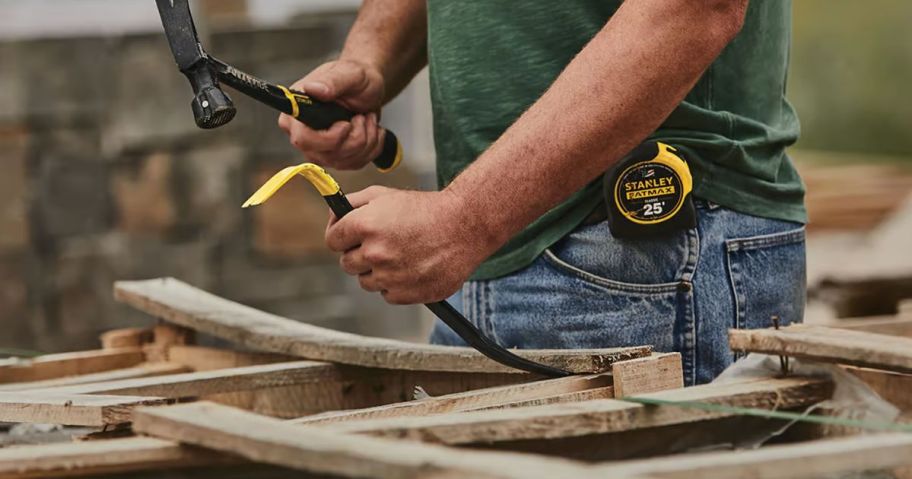 person using a hammer and small hand tool pry bar while working with wood