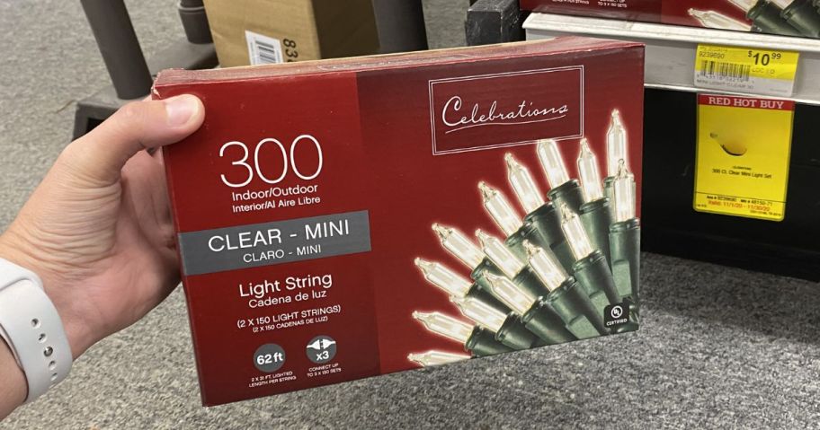 hand holding a box of clear Christmas lights, more on a shelf behind it