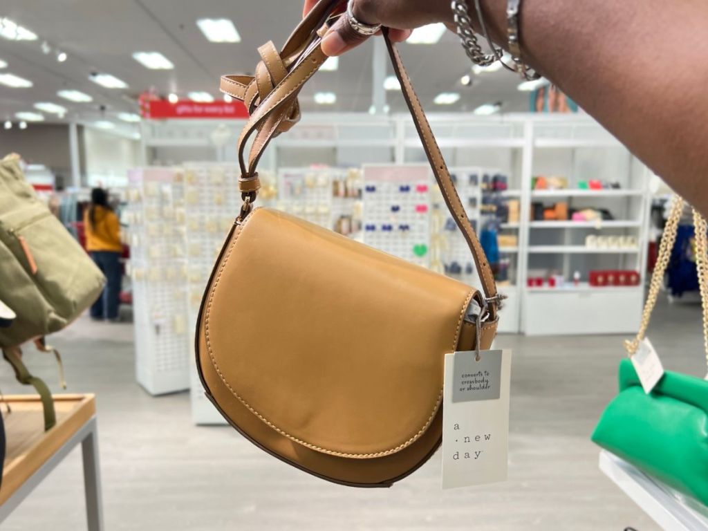 a womans hand displaying a A New Day Saddle Crossbody Bag in Brown