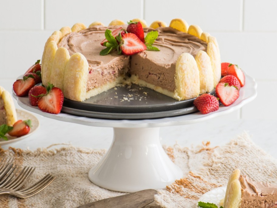 chocolate ice cream cake surrounded by lady fingers and strawberries on a white pedestal