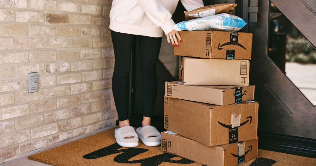 woman standing next to a stack of amazon boxes on porch