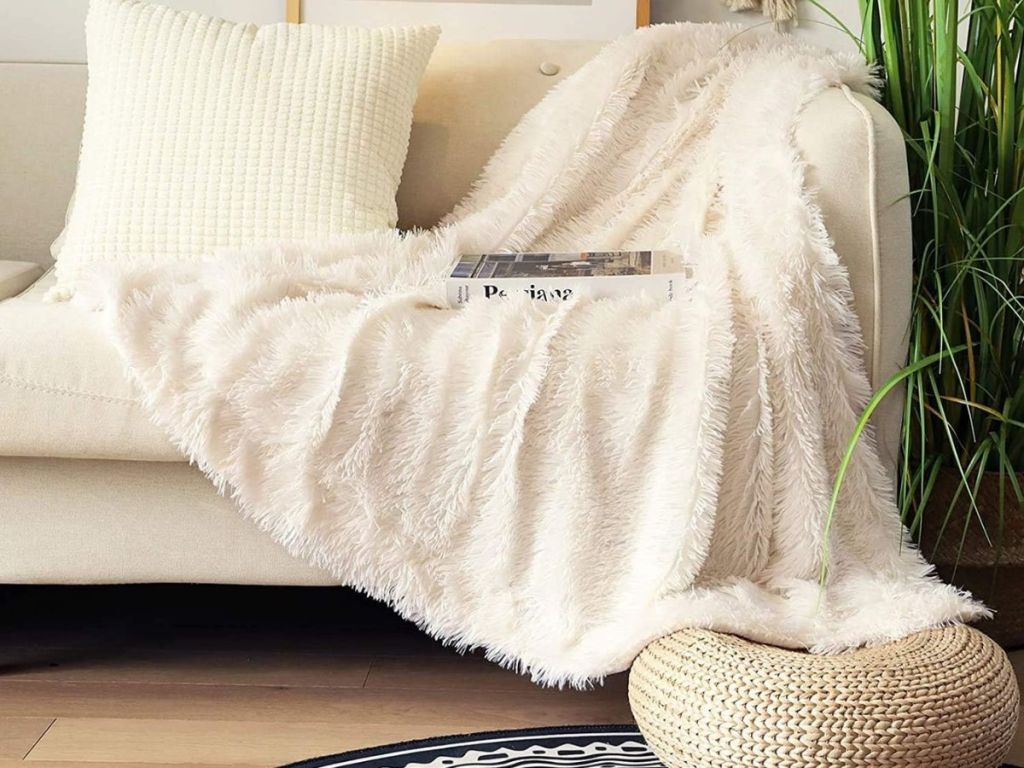 A white faux fur throw on a couch with boo set on the blanket