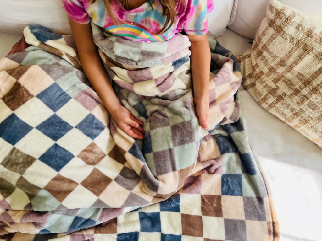 Little girl, sitting with big one checker board, blanket over her lap on couch
