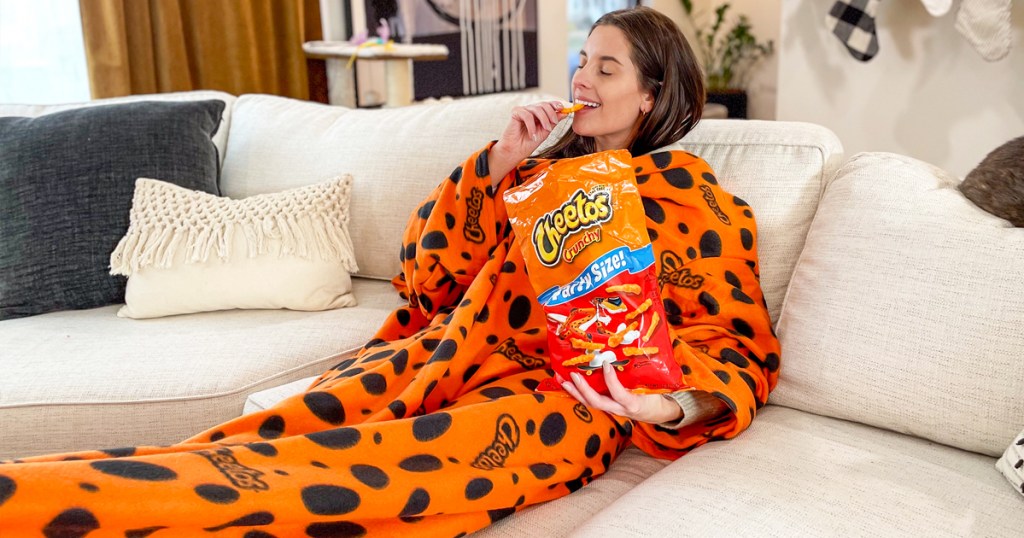 woman eating cheetos on couch under a cheetos print snuggie blanket