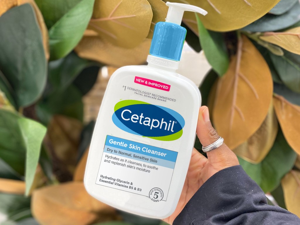hand holding a bottle of Cetaphil Hydrating Gentle Skin Cleanser with leaves in the background