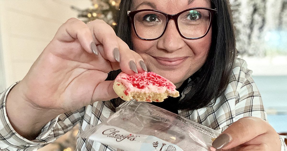 woman holding up a pink frosted cookie with sprinkles