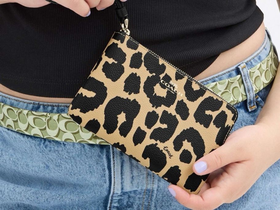 A woman holding a Coach Corner Zip Wristlet With Leopard Print