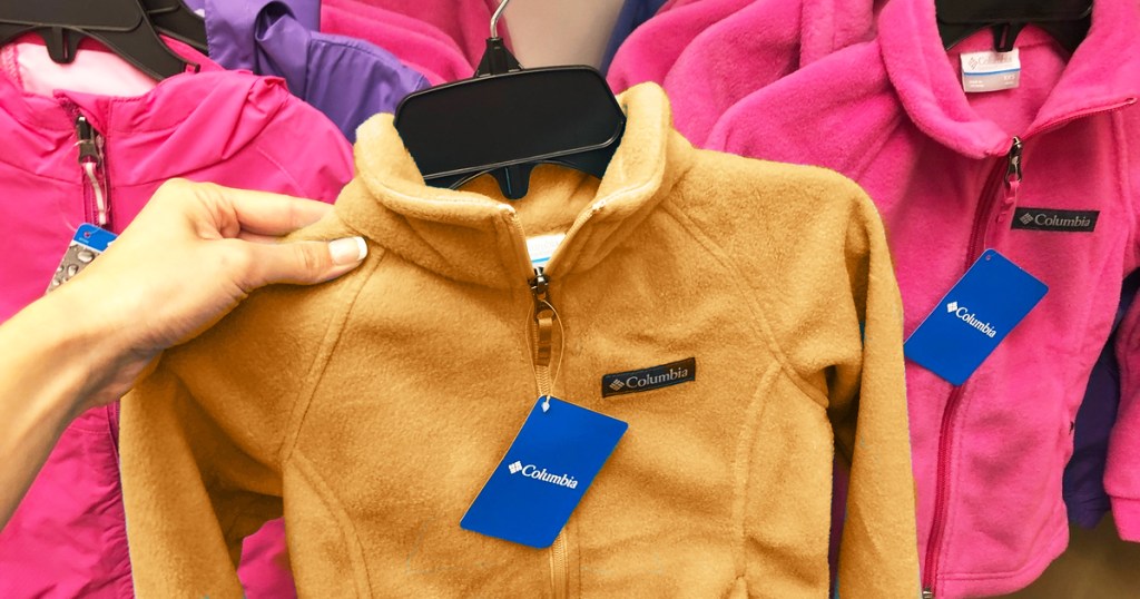 woman holding up orange columbia fleece jacket on hanger in store