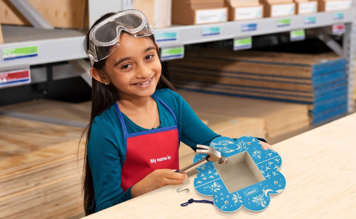 a little girl sitting at a work table displaying a Flower shaped Bird Feeder that she made in a lowes kids DIY workshop