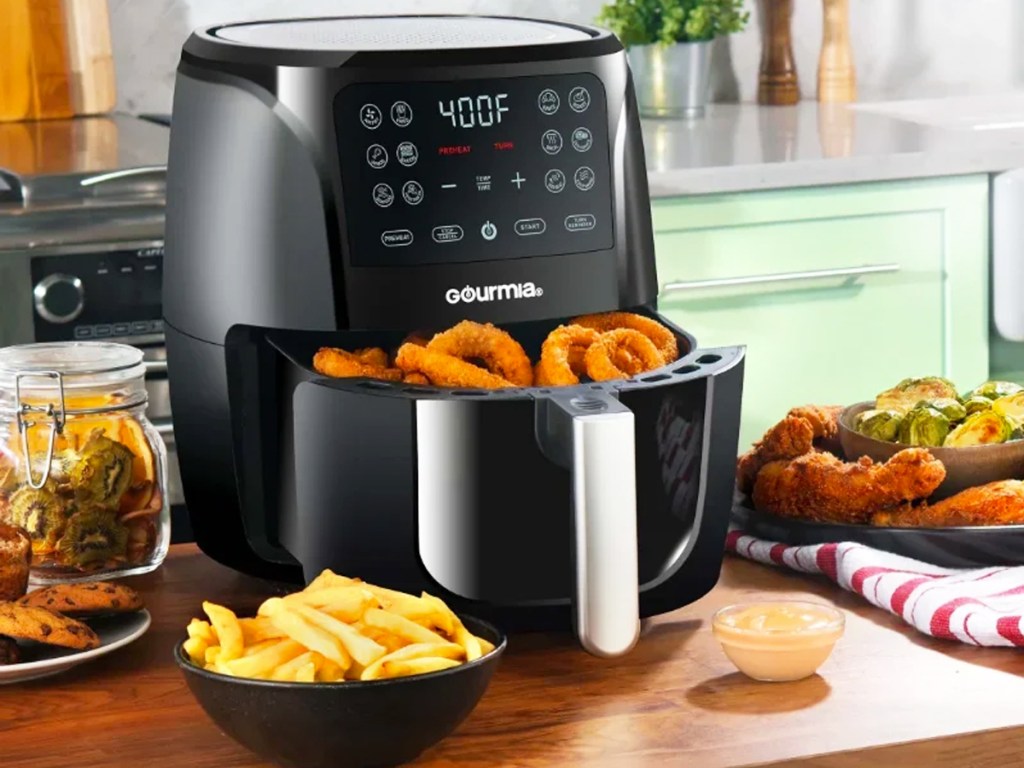 black air fryer with basket full of onion rings next to bowl of fries