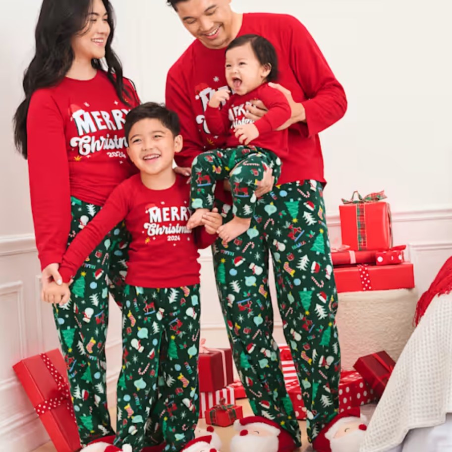 family with mom dad, little boy and baby wearing matching red and green Christmas pajamas that say 