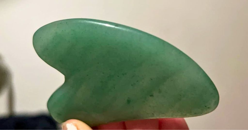 hand holding a green Gua Sha Jade Tool 