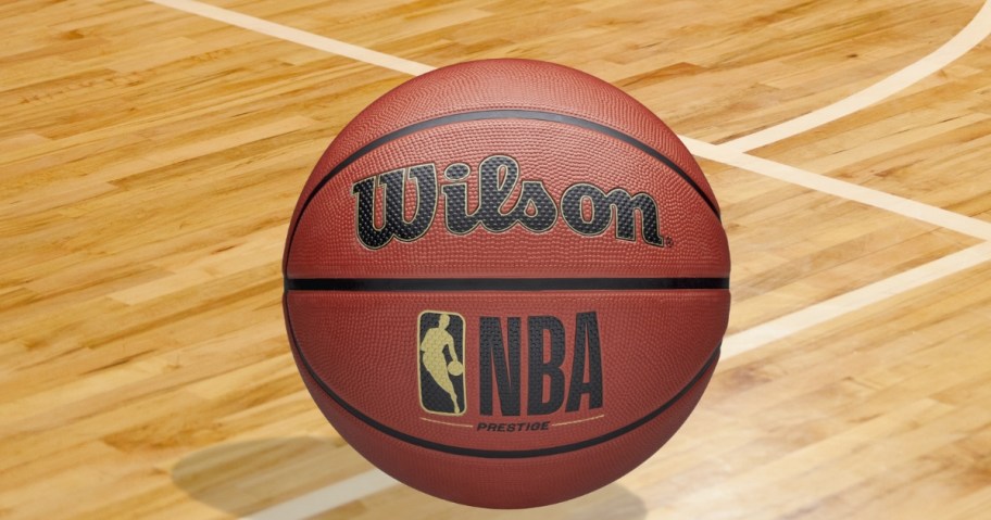 an orangish brown Wilson NBA basketball on a wood indoor basketball court floor