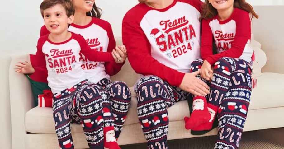 family sitting on a couch wearing matching blue, red and white Christmas pajamas that say 