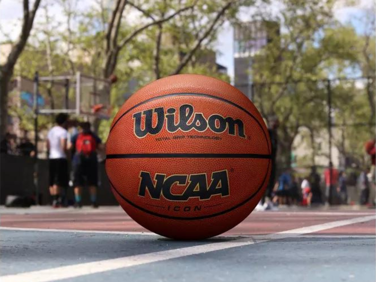a basketball court with people playing in the background, and the Wilson Icon basketball in the center
