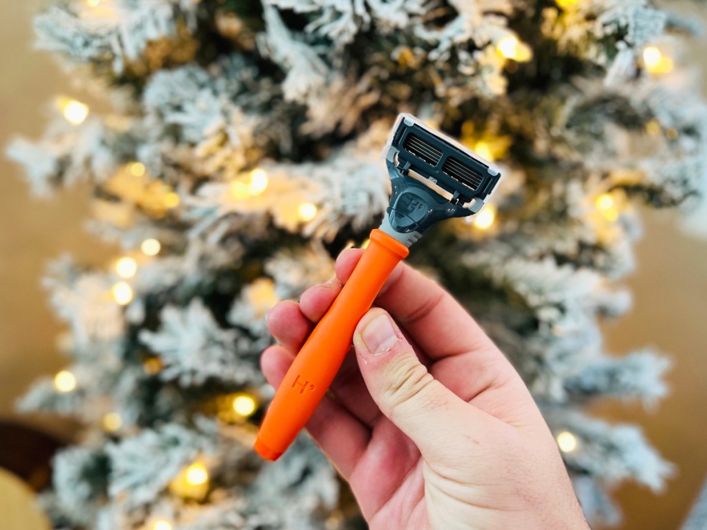 holding an orange and black razor in front of christmas tree