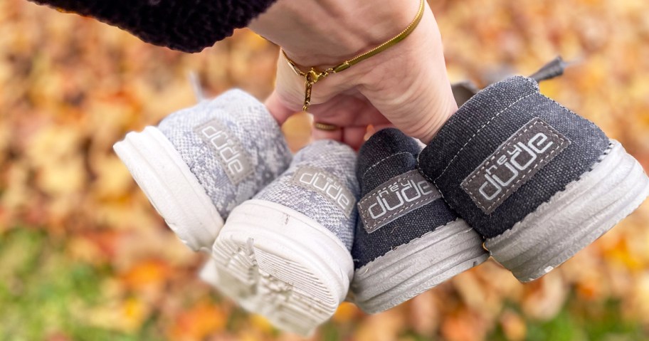 hand holding two pairs of hey dude sneakers