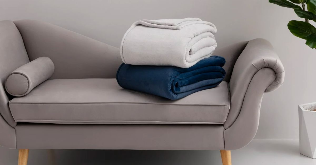 2 Hotel Style Luxury Plush Blankets one in navy and one in gray, stacked on a love seat