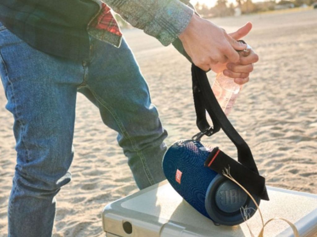 JBL Xtreme 2 speaker with someone using the bottle opener on the strap to open a drink