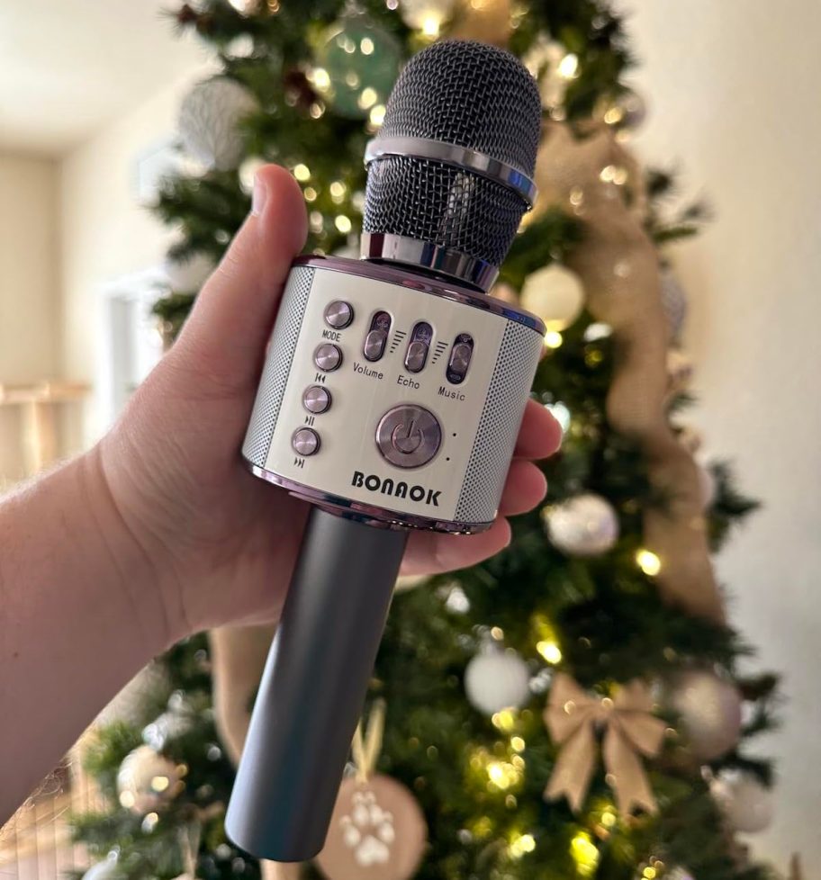 Hand holding a karaoke microphone in front of Christmas tree