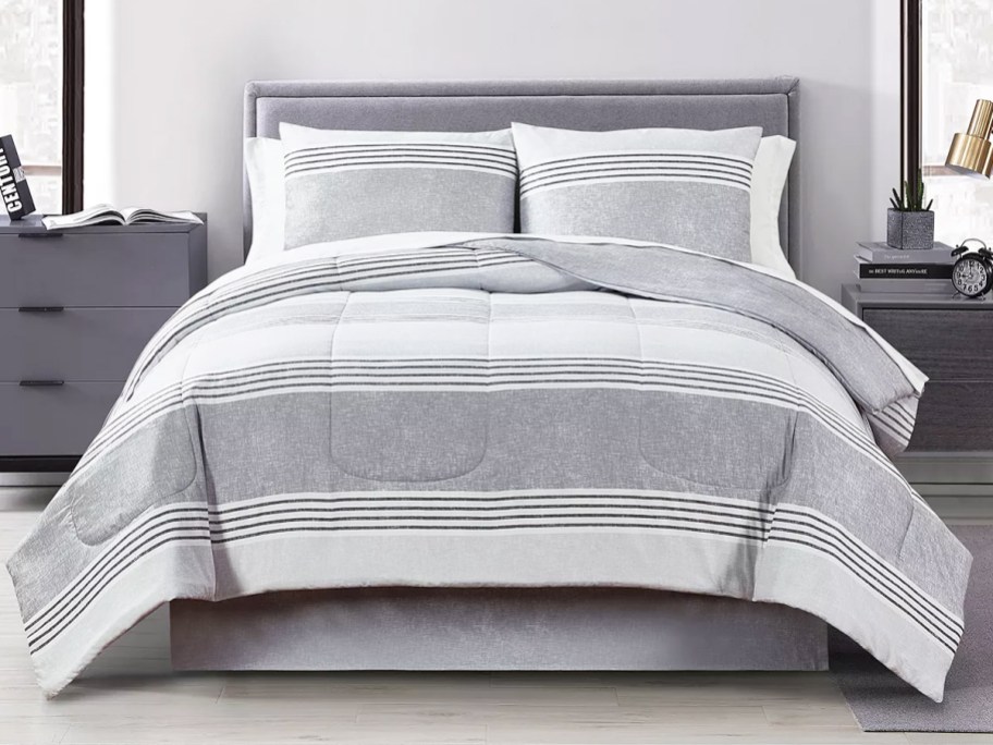 grey and white striped comforter on a bed with grey headboard and furniture