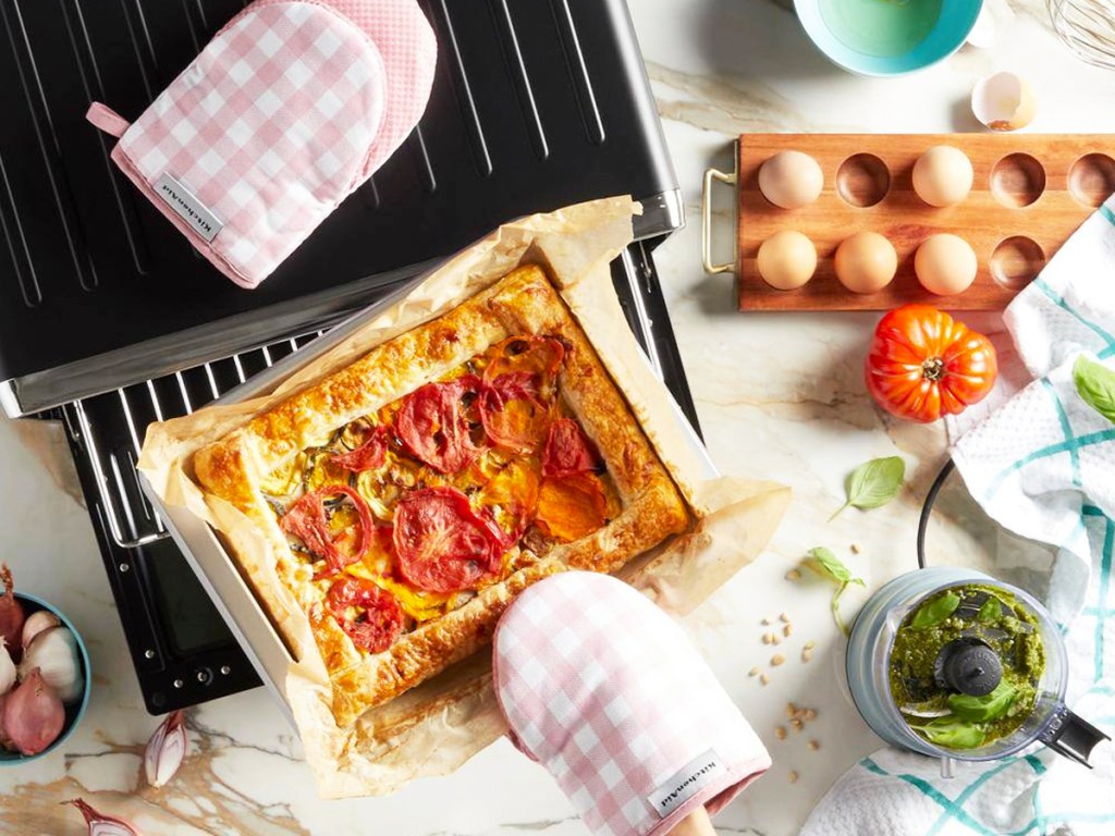 using pink and white gingham oven mitts to take pizza out from oven