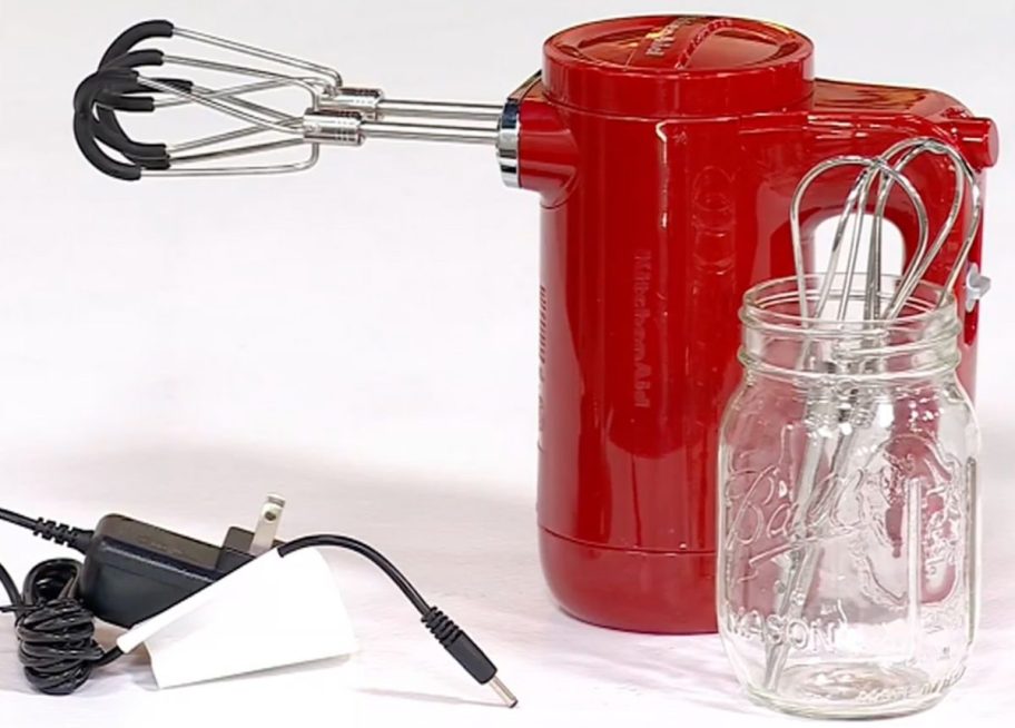 A red Kitchenaid Cordless Miser with flex Edge Beaters and the charging cord and a mason charge with the Turbo beaters set inside of it