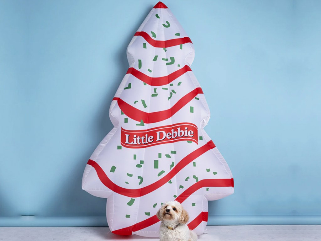 white and red Little Debbie Christmas Tree Cake Inflatable with dog sitting in front of it