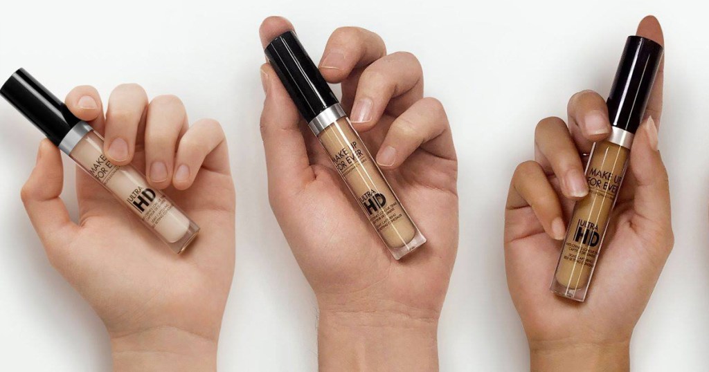 three hands holding tubes of concealer