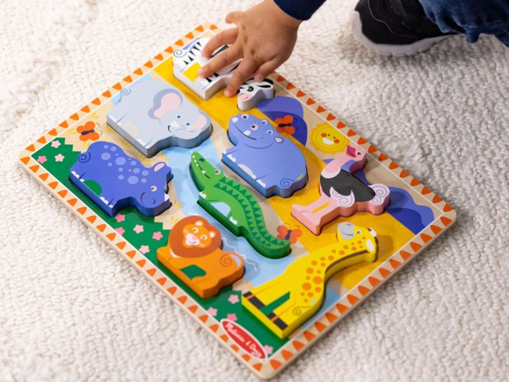 A Melissa & Doug Chunky Puzzle with Safari Animals with a child's hand touching one of the pieces