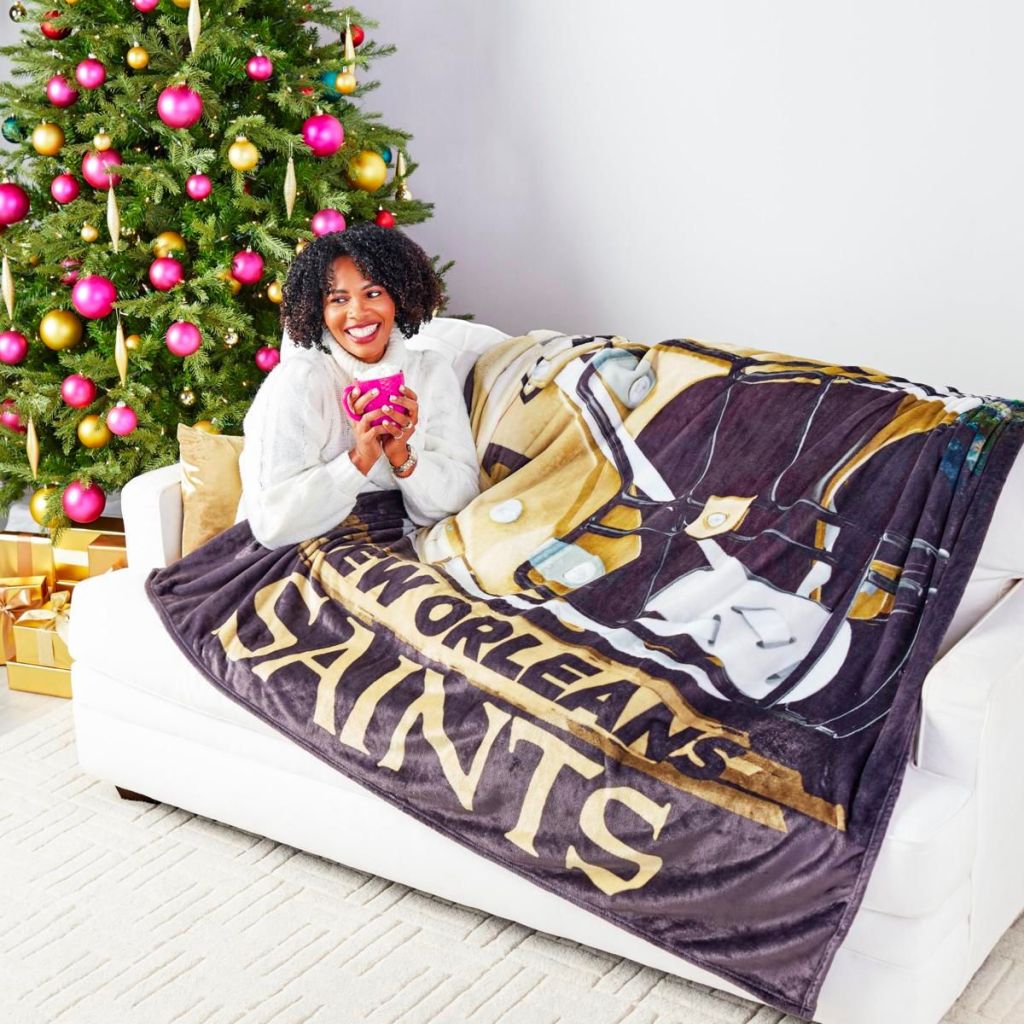 A woman on a sofa covered up with a new orleans saints oversized throw spread across a sofa