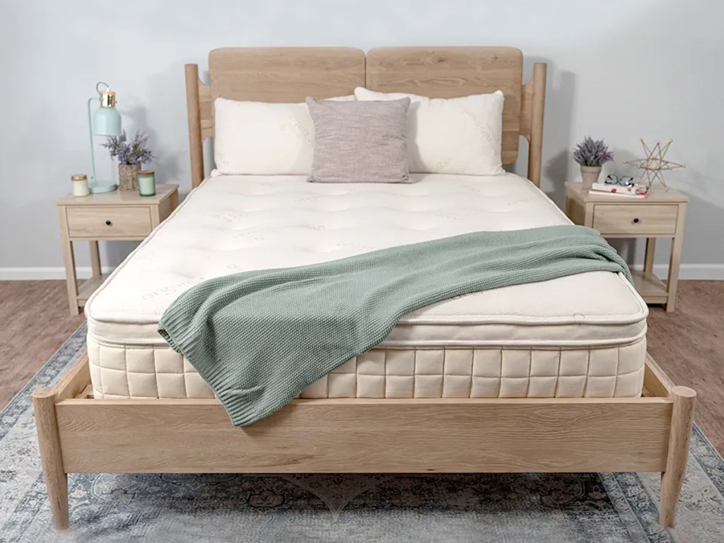 pillowtop mattress on a light wood bed frame with throw blanket draped across it