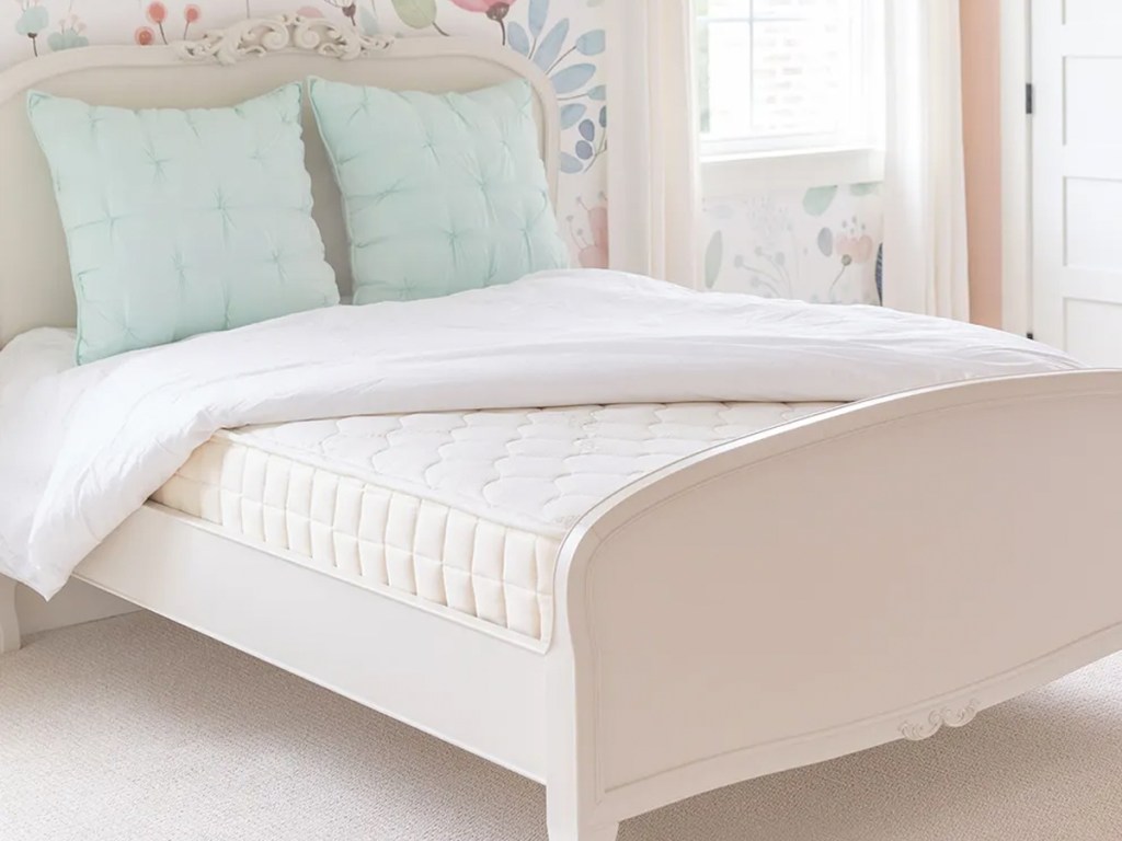 mattress on a white bed frame with white head and footboards and blue pillows
