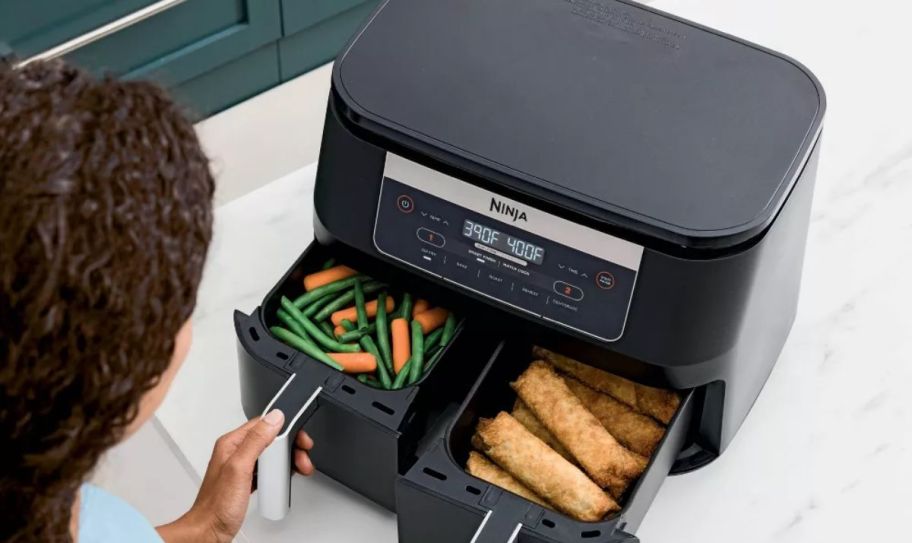 a Ninja Foodi air fryer on a kitchen counter with cooked food in both baskets