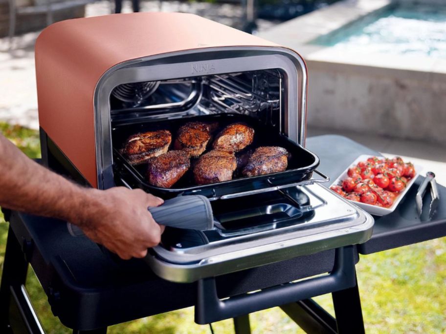 person taking chicken breasts out of Ninja Woodfire Outdoor Oven
