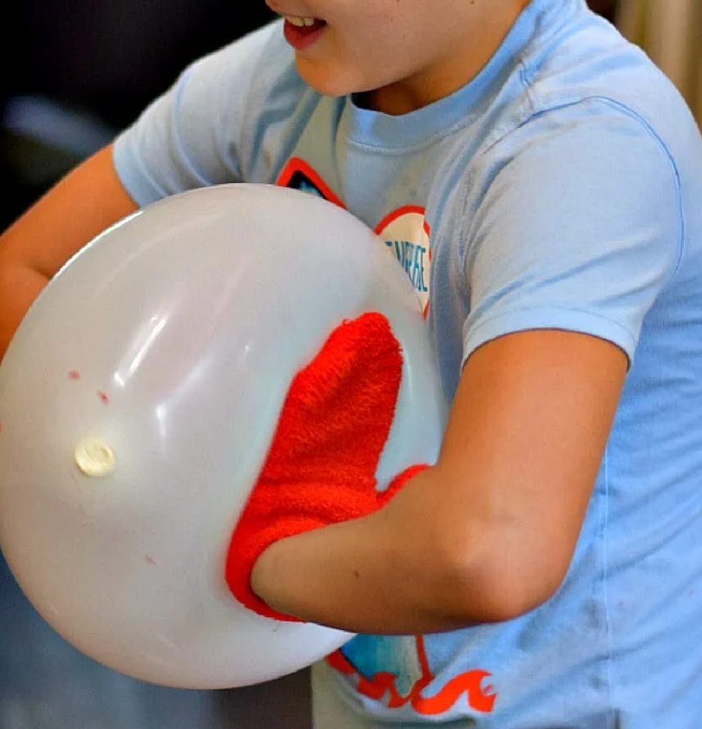 a boy trying to pop a balloon while wearing mittens