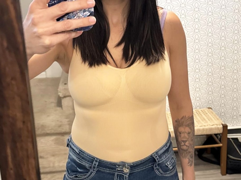 woman taking photo in mirror wearing bodysuit and jeans