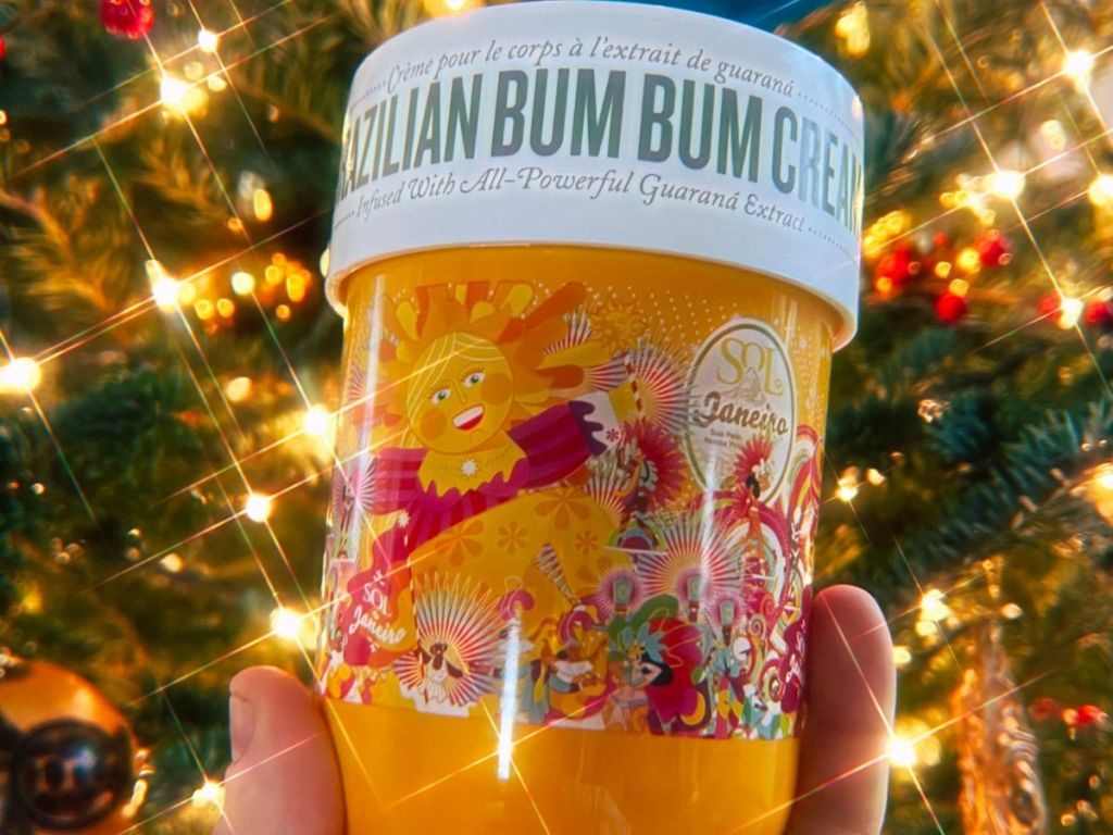 A super size jar of Sol De Janiero Bum Bum cream held up in front of a Christmas Tree