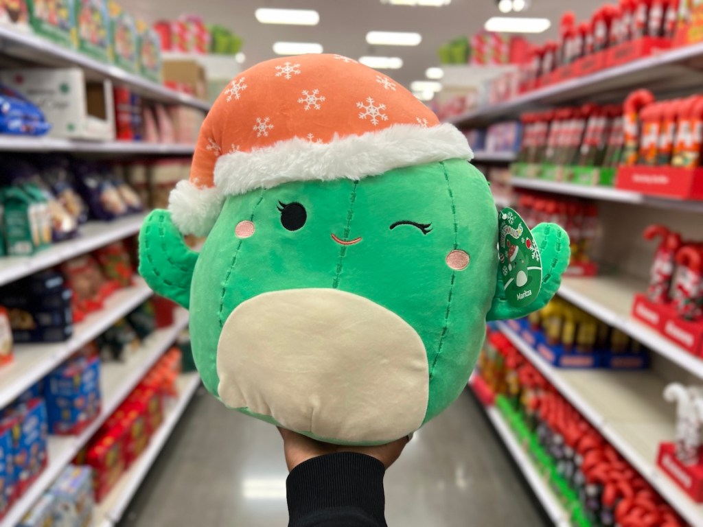 Hand holding a green cactus squishmallow with Santa hat in target store aisle