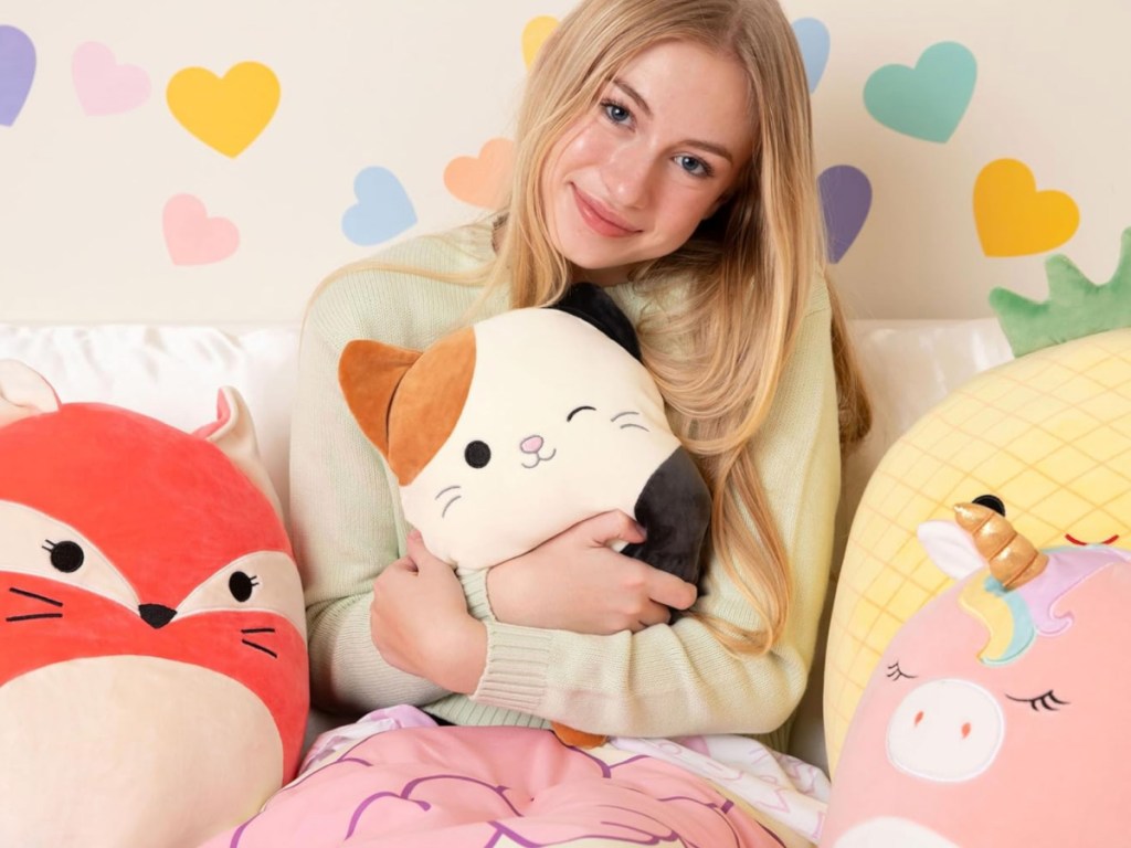 blond teen girl hugging Squishmallows Cam Heating Pad in bed