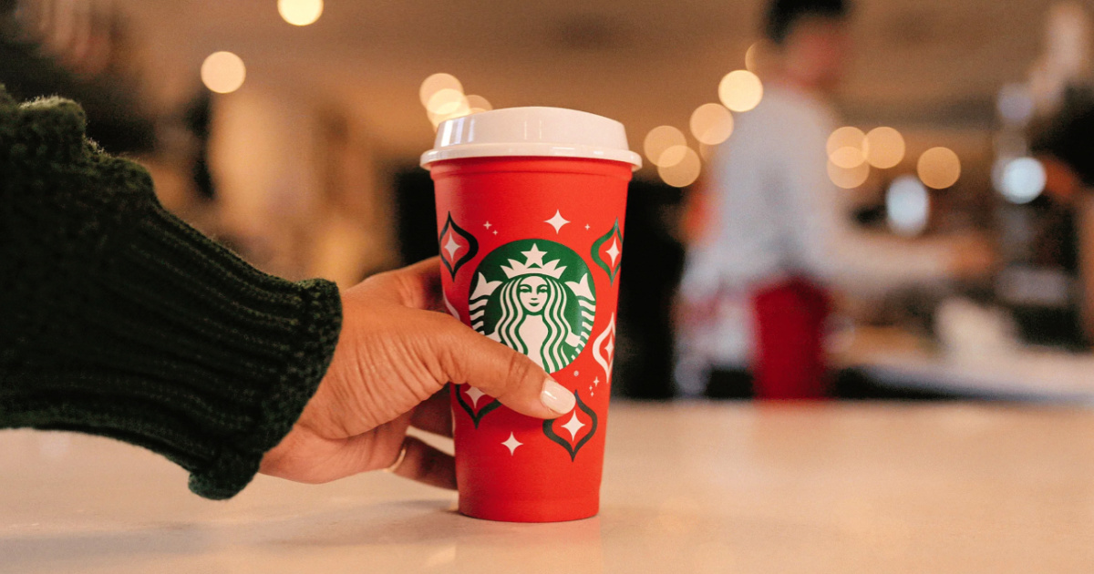person grabbing starbucks red cup from counter
