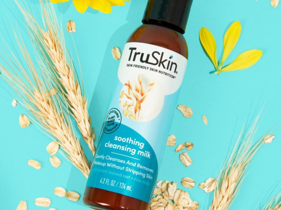 bottle of TruSkin Soothing Cleansing Milk near wheat, oats, and flowers